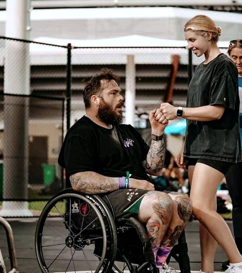 An adaptive CrossFit athlete in a wheelchair fist-bumping a support worker at a competition.